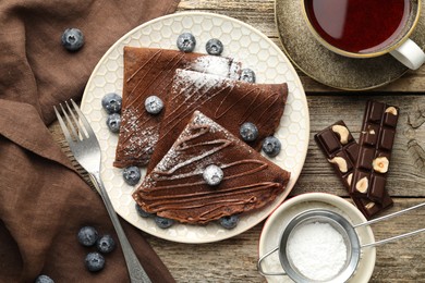 Photo of Delicious chocolate crepes with blueberries served on wooden table, flat lay