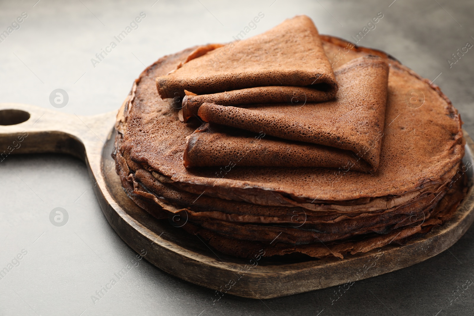 Photo of Stack of delicious chocolate crepes on grey table, closeup