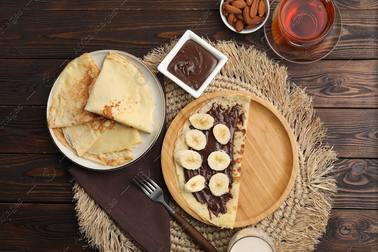 Photo of Delicious crepes with chocolate paste and banana served on wooden table, flat lay