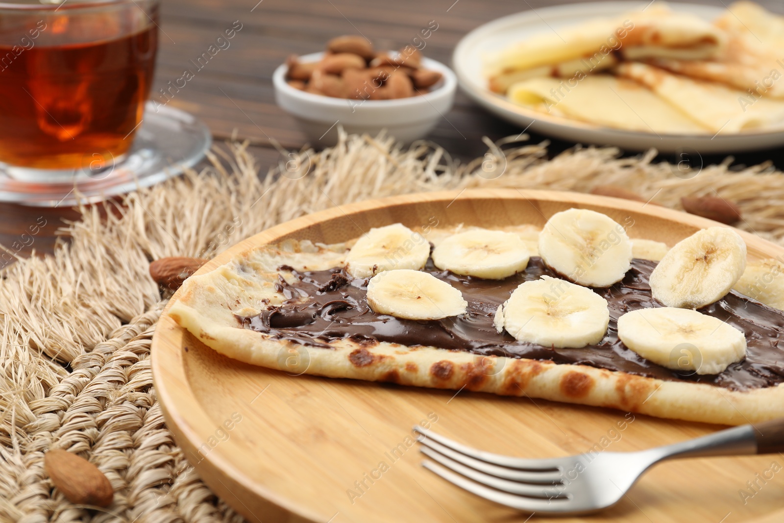 Photo of Delicious crepe with chocolate paste, banana and almonds served on wooden table, closeup