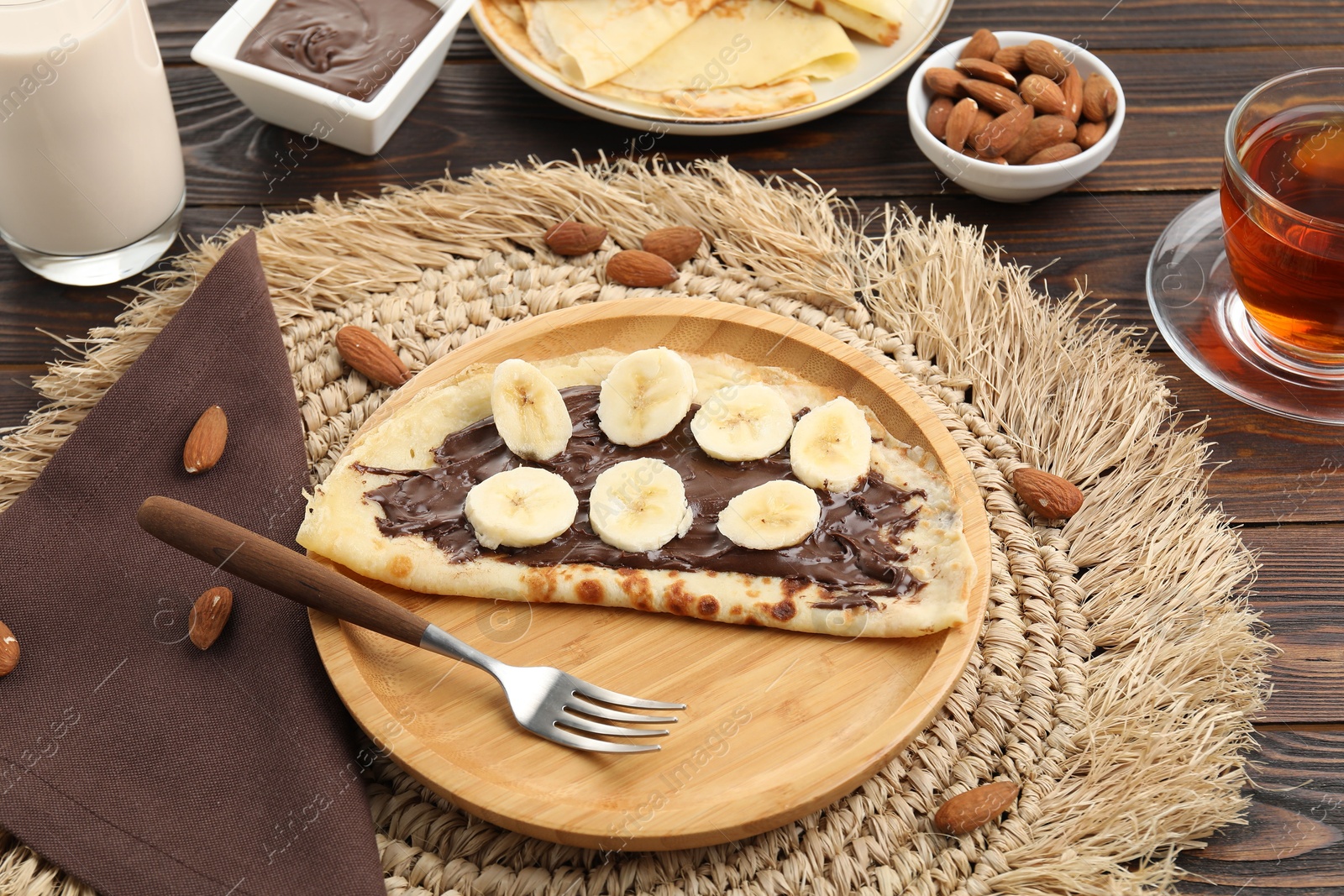 Photo of Delicious crepe with chocolate paste, banana and almonds served on wooden table, closeup