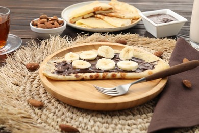 Delicious crepe with chocolate paste, banana and almonds served on wooden table, closeup