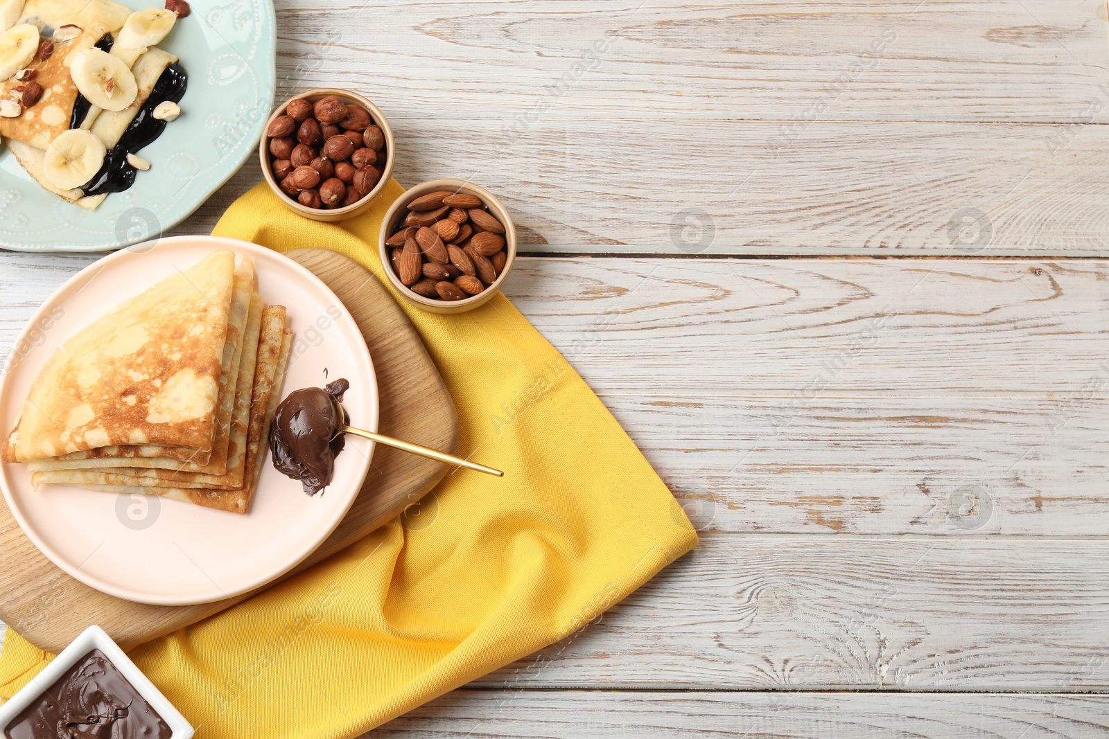 Photo of Delicious crepes served with chocolate paste and nuts on wooden table, flat lay. Space for text