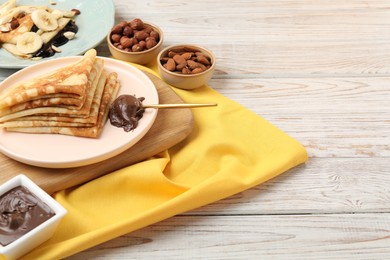 Delicious crepes served with chocolate paste and nuts on wooden table, space for text