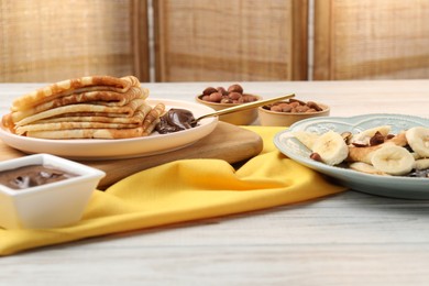 Photo of Delicious crepes served with chocolate paste and nuts on wooden table, closeup