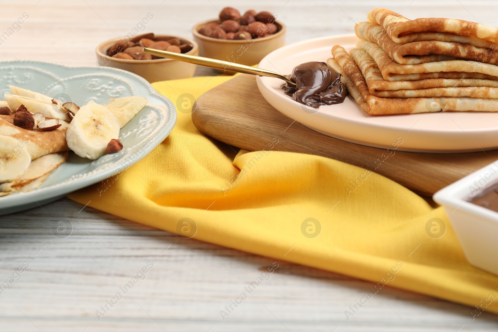 Photo of Delicious crepes served with chocolate paste and nuts on wooden table, closeup