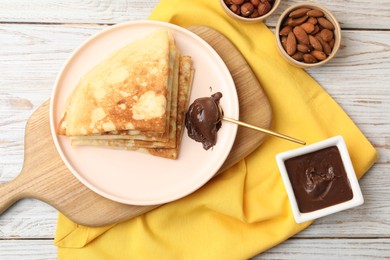 Photo of Delicious crepes with chocolate paste and nuts on wooden table, flat lay