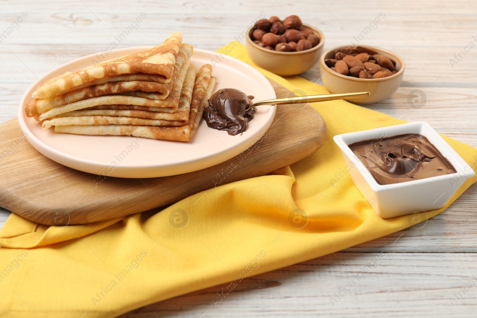 Photo of Delicious crepes with chocolate paste and nuts on wooden table, closeup