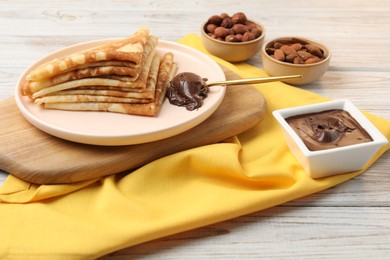 Photo of Delicious crepes with chocolate paste and nuts on wooden table, closeup