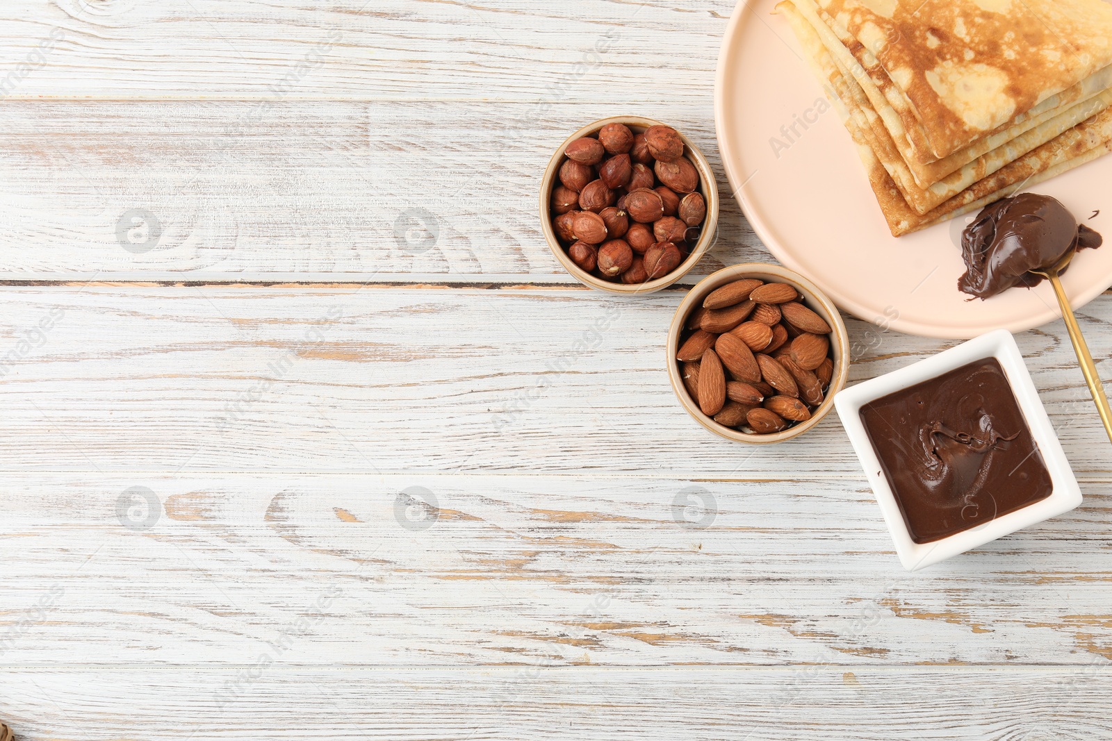 Photo of Delicious crepes with chocolate paste and nuts on wooden table, flat lay. Space for text