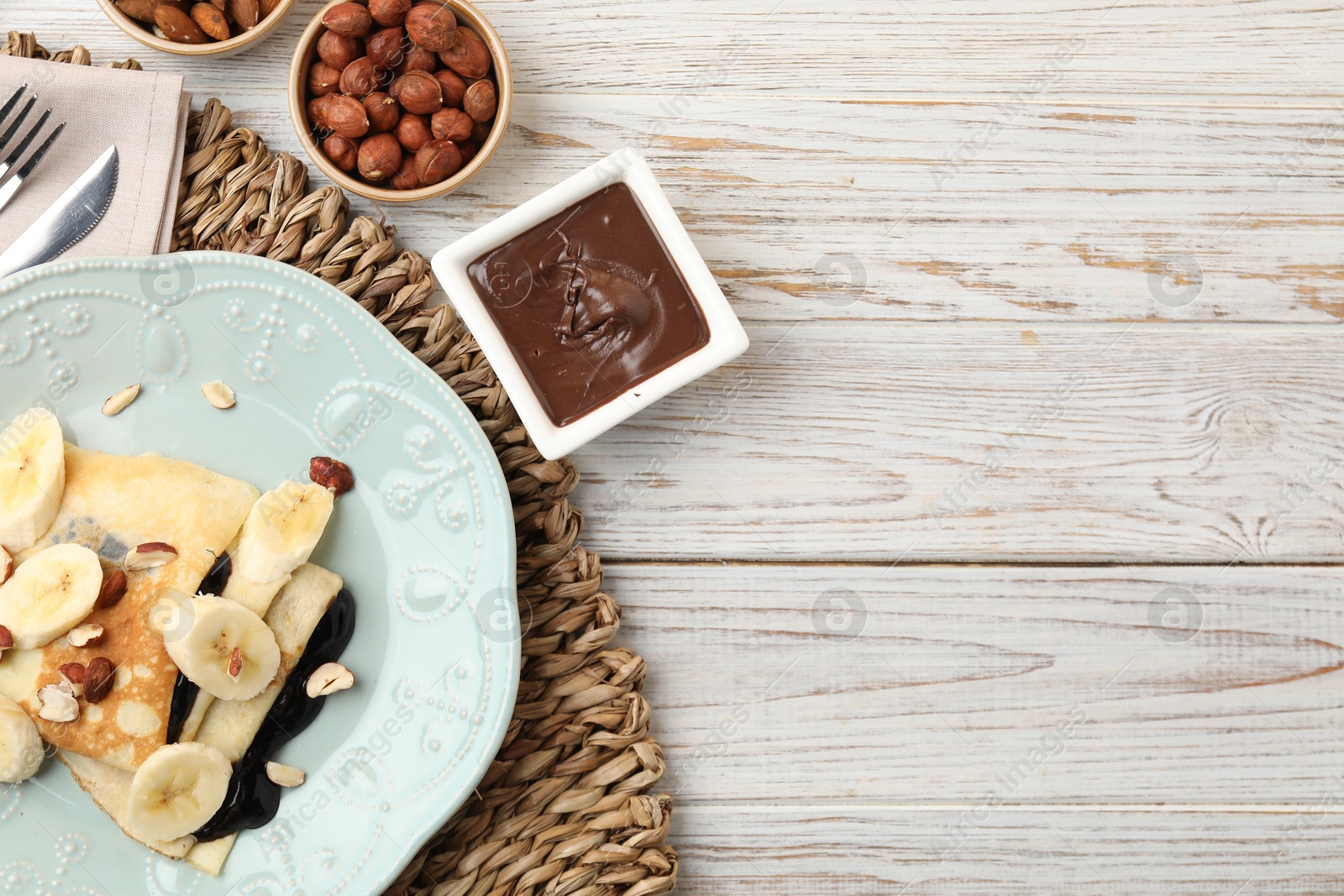 Photo of Delicious crepes with banana, chocolate sauce and nuts on wooden table, flat lay. Space for text