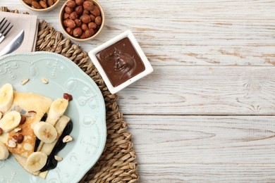 Photo of Delicious crepes with banana, chocolate sauce and nuts on wooden table, flat lay. Space for text