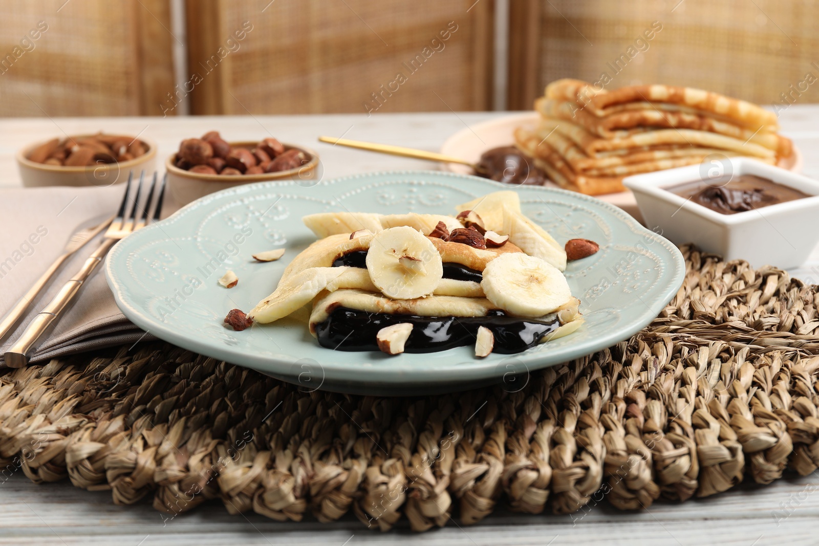 Photo of Delicious crepes with banana, chocolate sauce and nuts on wooden table, closeup