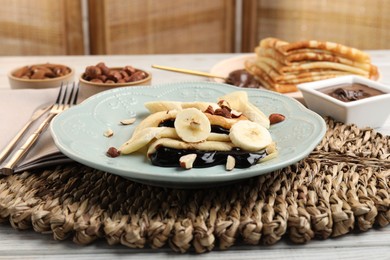 Photo of Delicious crepes with banana, chocolate sauce and nuts on wooden table, closeup