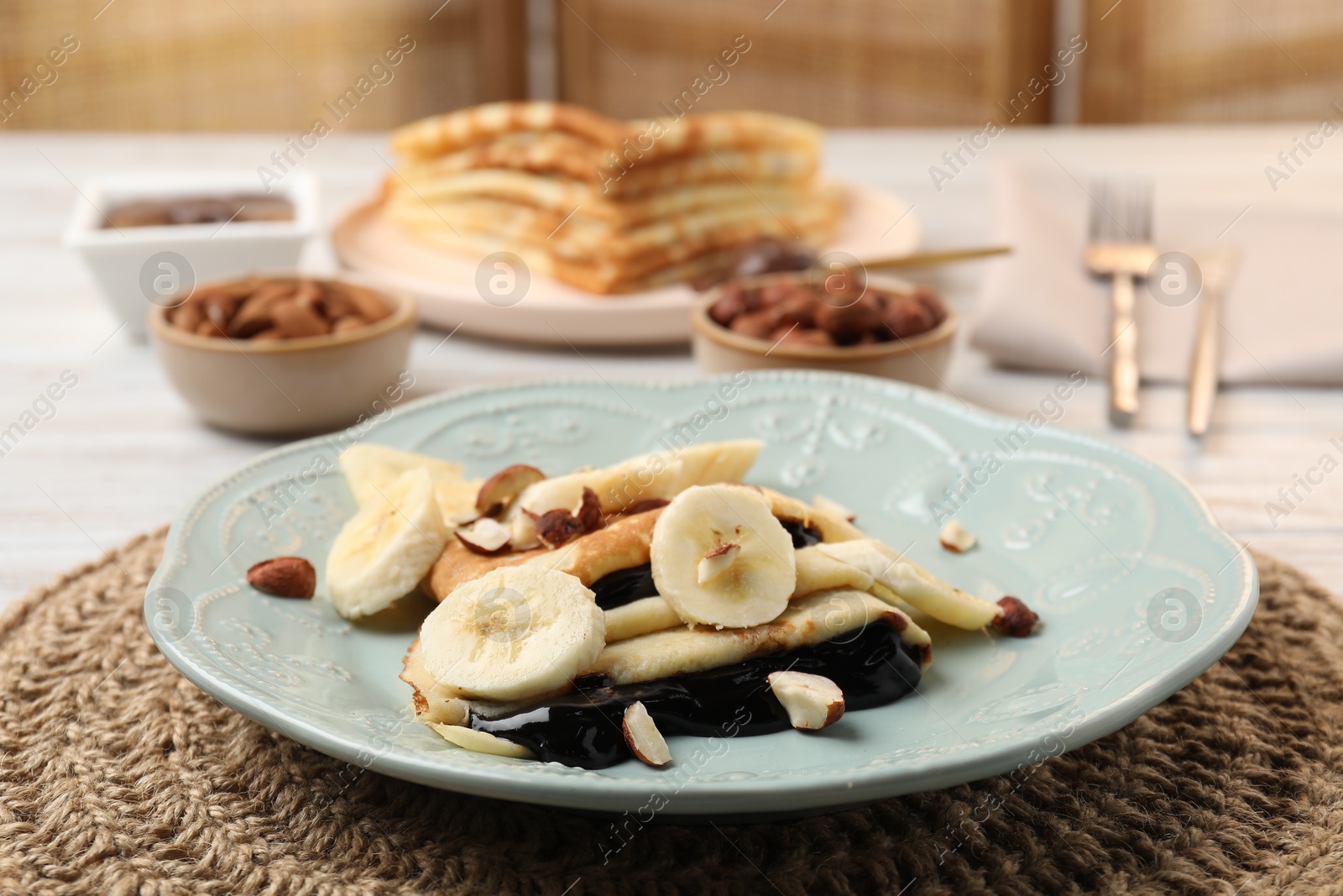 Photo of Delicious crepes with banana, chocolate sauce and nuts on table, closeup