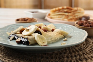 Delicious crepes with banana, chocolate sauce and nuts on table, closeup