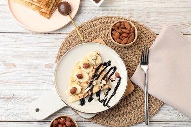 Delicious crepes served with chocolate sauce and nuts on wooden table, flat lay