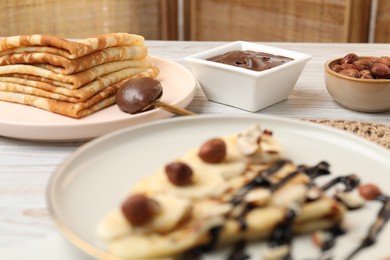 Delicious crepes with nuts and chocolate sauce on wooden table, closeup