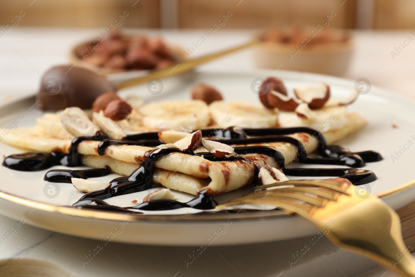 Photo of Delicious crepe with banana, nuts and chocolate sauce on table, closeup