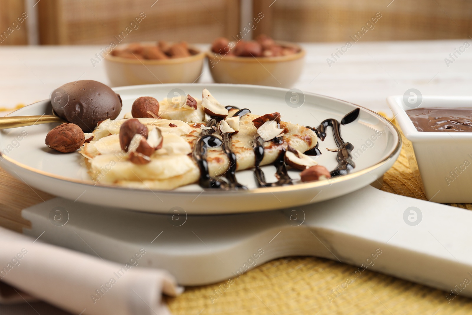 Photo of Delicious crepe with banana, nuts and chocolate sauce on table, closeup