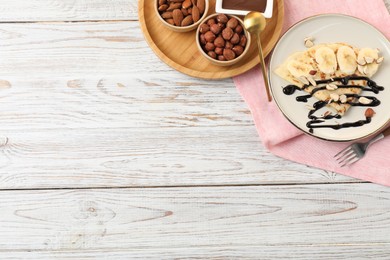 Photo of Delicious crepe with banana, nuts and chocolate sauce on wooden table, flat lay. Space for text