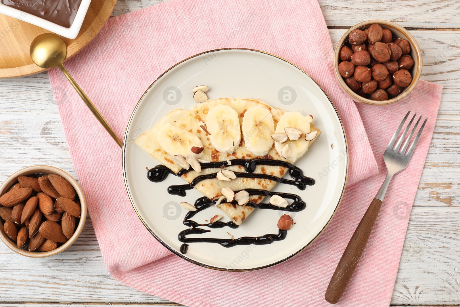 Photo of Delicious crepe with banana, nuts and chocolate sauce on wooden table, flat lay