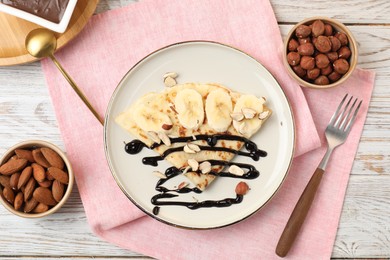 Delicious crepe with banana, nuts and chocolate sauce on wooden table, flat lay