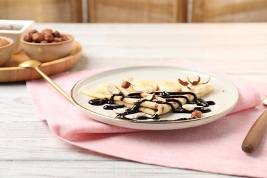 Delicious crepe with banana, nuts and chocolate sauce on wooden table, closeup