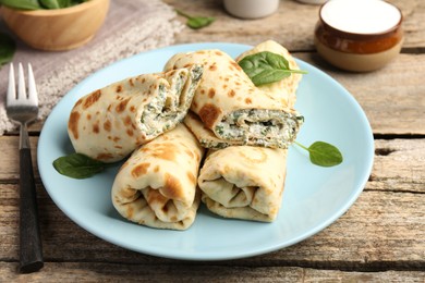 Photo of Tasty rolled crepes with cottage cheese and spinach served on wooden table, closeup