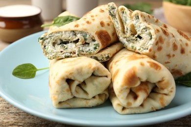 Photo of Tasty rolled crepes with cottage cheese and spinach served on wooden table, closeup