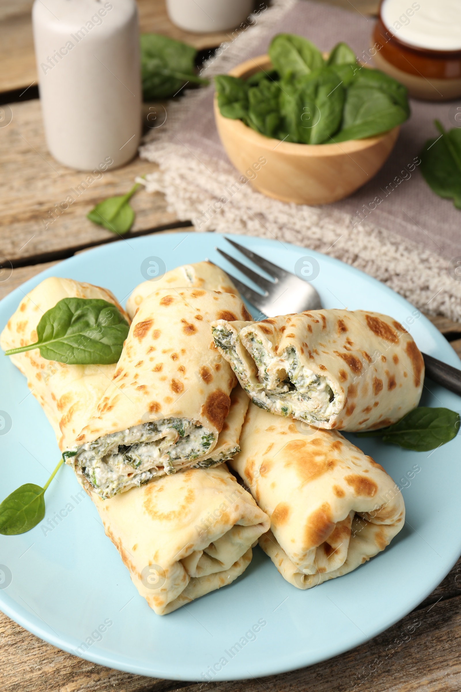 Photo of Tasty rolled crepes with cottage cheese and spinach served on wooden table, closeup