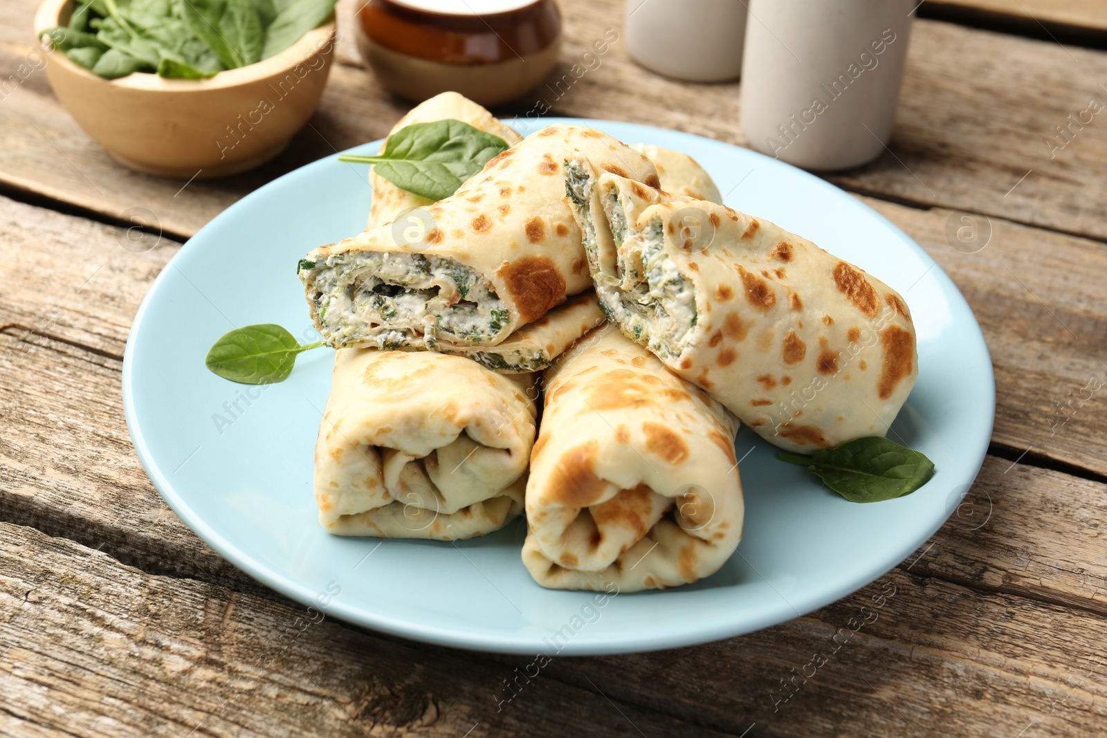 Photo of Tasty rolled crepes with cottage cheese and spinach served on wooden table, closeup