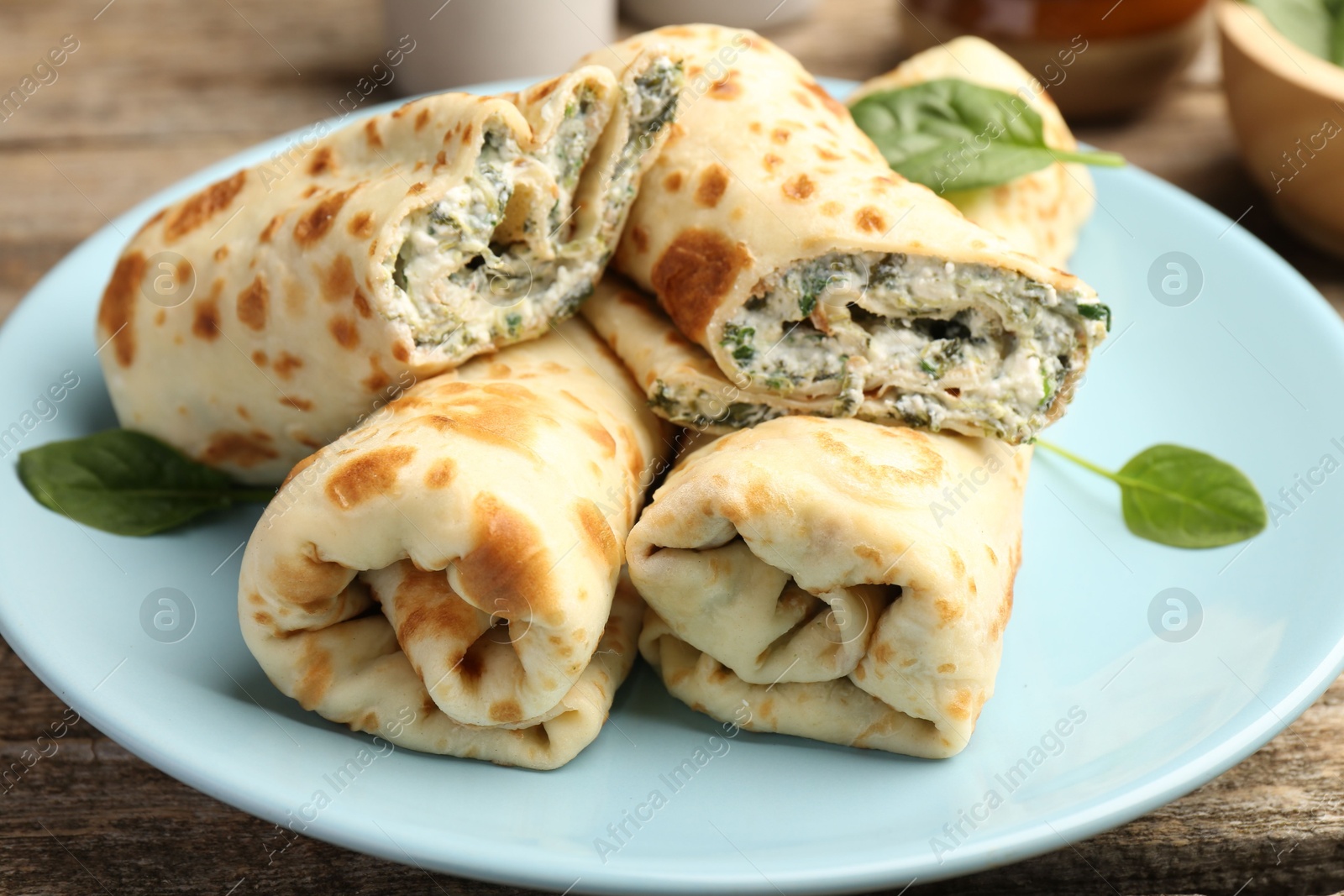 Photo of Tasty rolled crepes with cottage cheese and spinach served on wooden table, closeup