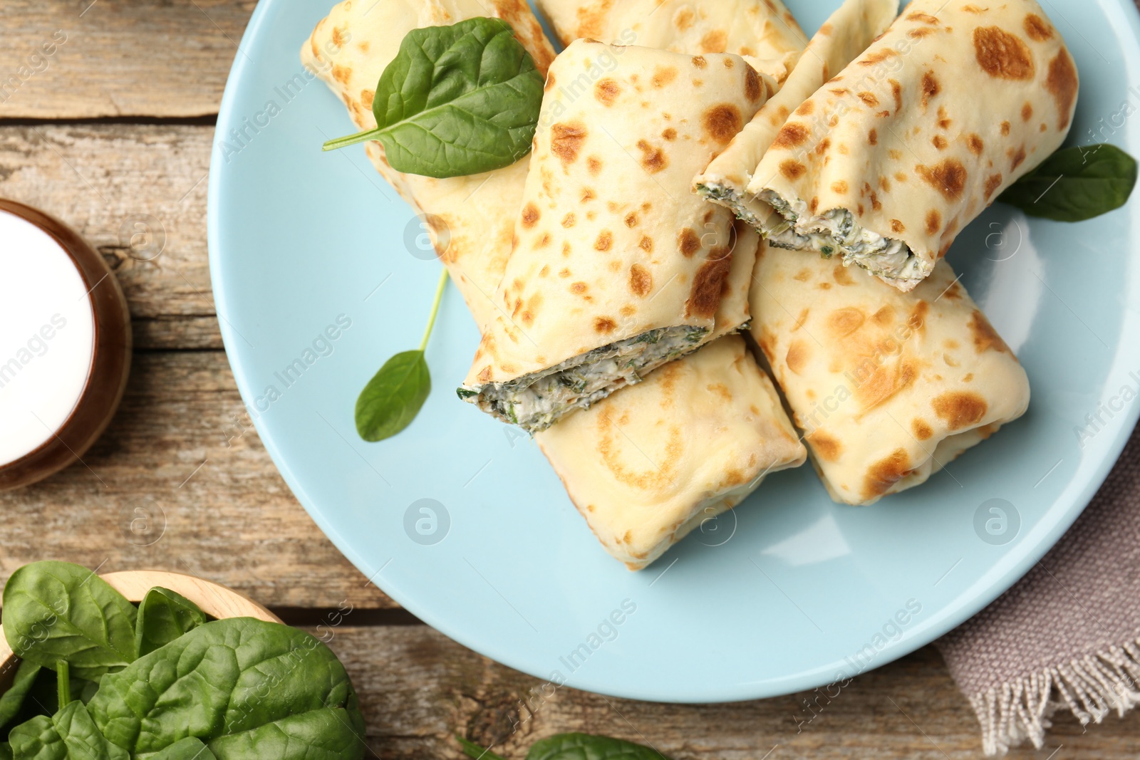 Photo of Tasty rolled crepes with cottage cheese and spinach served on wooden table, flat lay