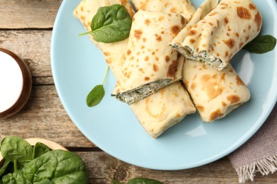 Photo of Tasty rolled crepes with cottage cheese and spinach served on wooden table, flat lay