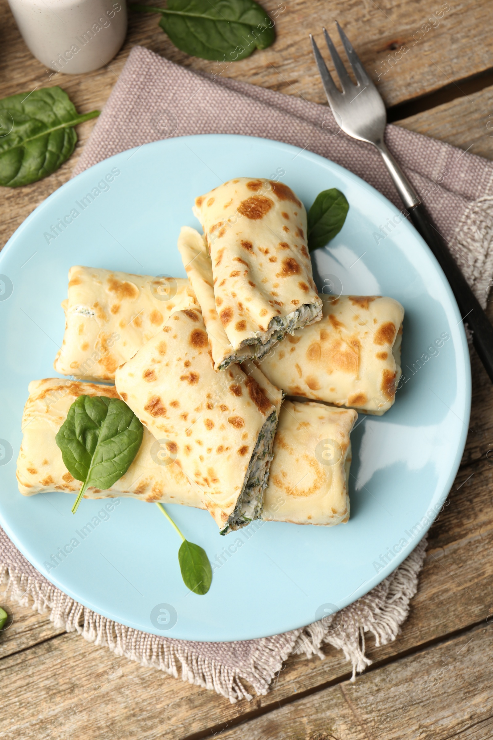 Photo of Tasty rolled crepes with cottage cheese and spinach served on wooden table, flat lay