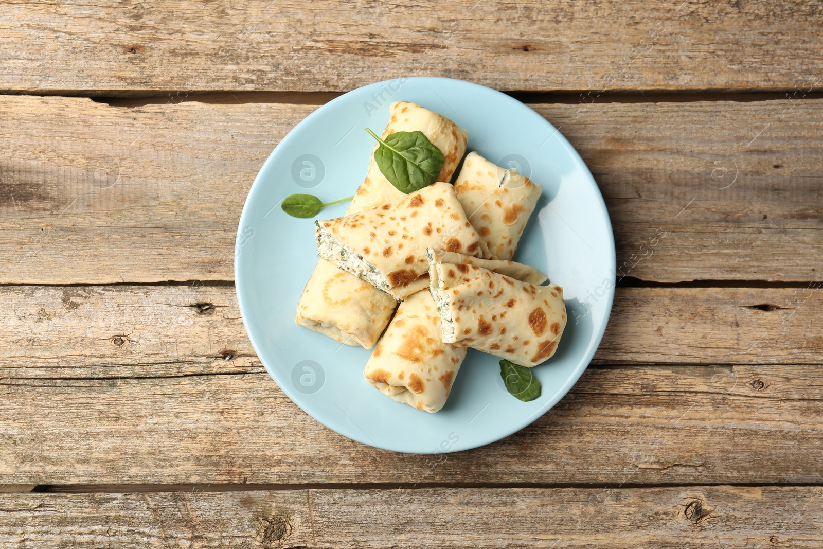 Photo of Tasty rolled crepes with cottage cheese and spinach served on wooden table, top view