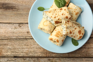 Photo of Tasty rolled crepes with cottage cheese and spinach served on wooden table, top view. Space for text