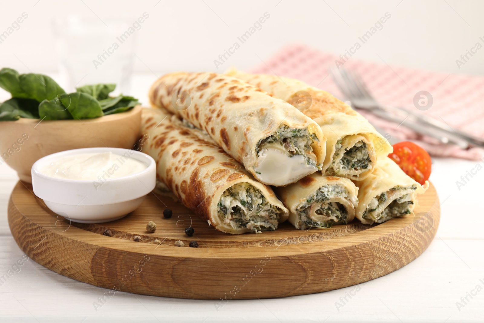 Photo of Tasty rolled crepes with cottage cheese and spinach served on white wooden table, closeup