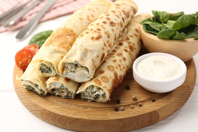 Photo of Tasty rolled crepes with cottage cheese and spinach served on white wooden table, closeup