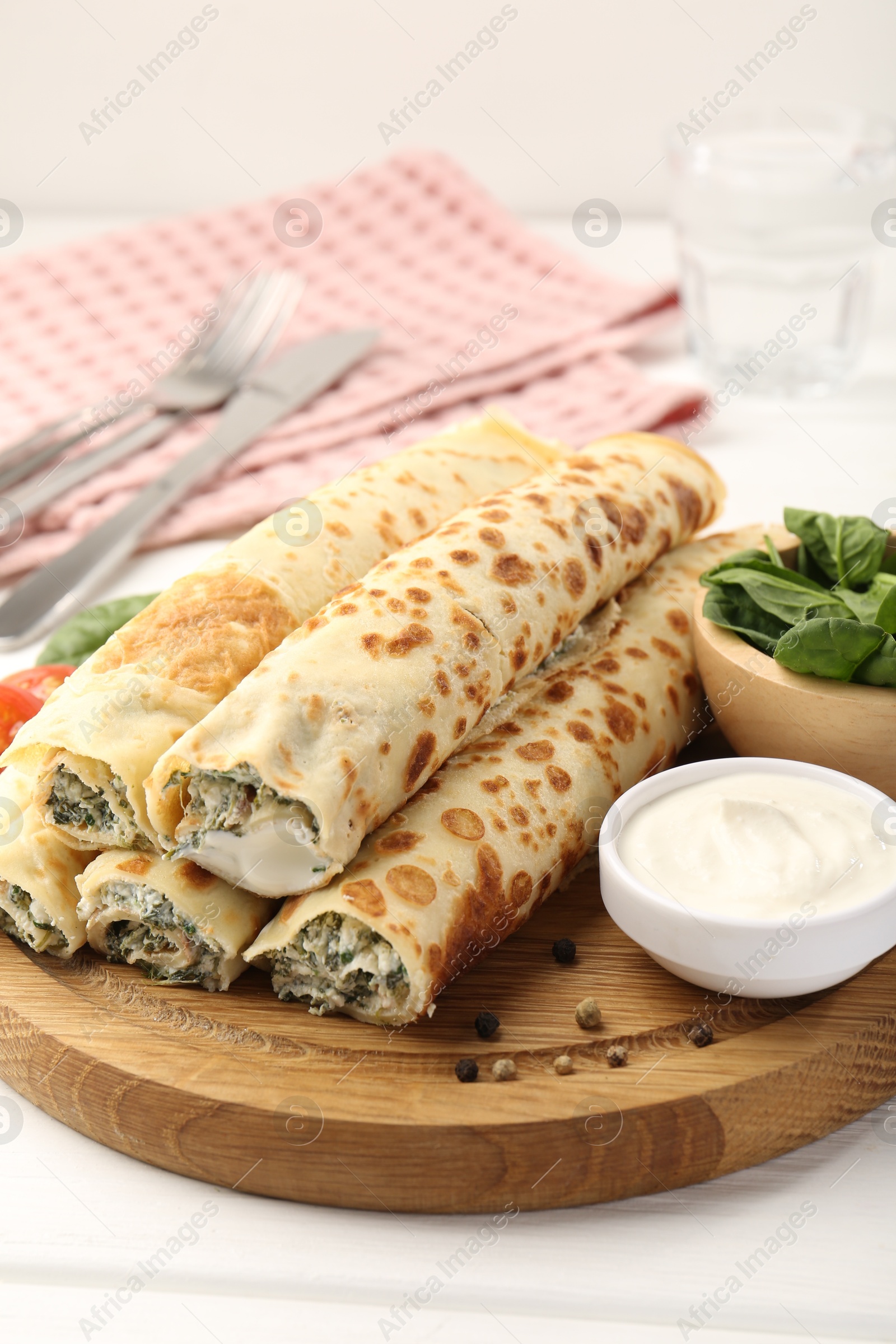 Photo of Tasty rolled crepes with cottage cheese and spinach served on white wooden table, closeup