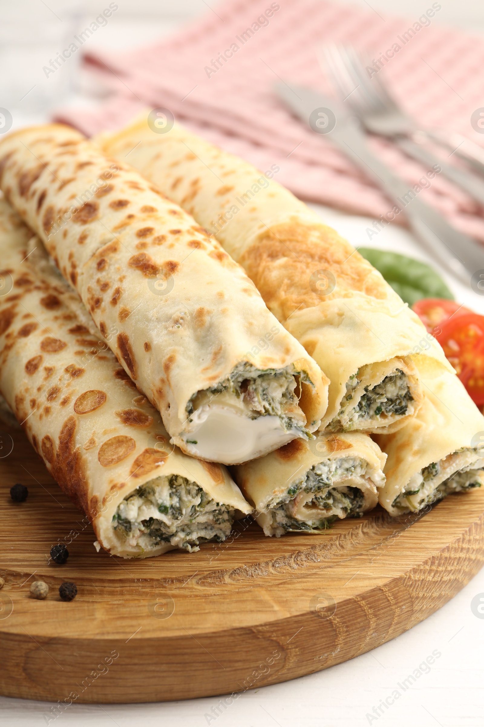 Photo of Tasty rolled crepes with cottage cheese and spinach served on white wooden table, closeup