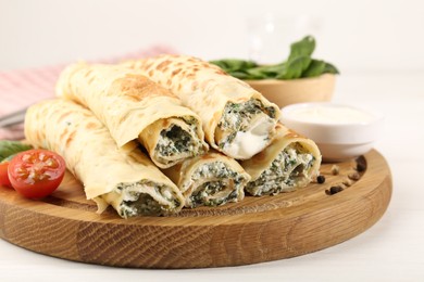 Photo of Tasty rolled crepes with cottage cheese and spinach served on white wooden table, closeup