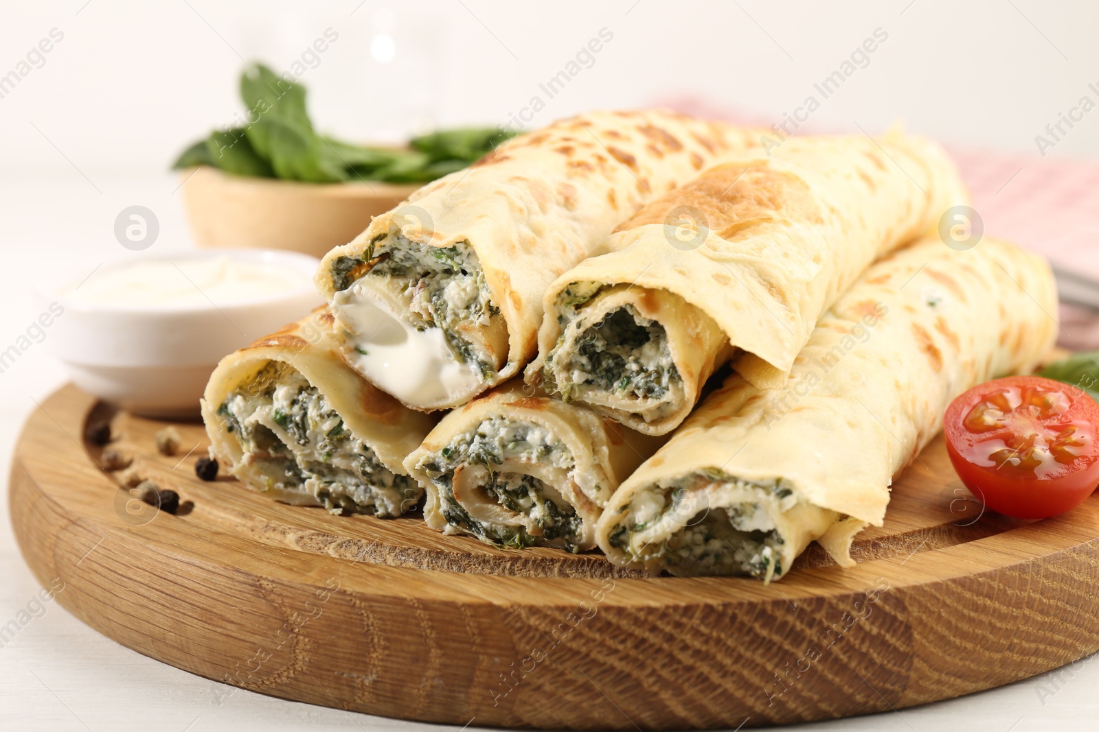 Photo of Tasty rolled crepes with cottage cheese and spinach served on white wooden table, closeup