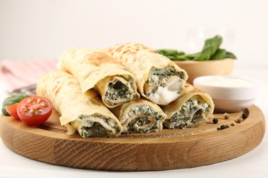 Photo of Tasty rolled crepes with cottage cheese and spinach served on white wooden table, closeup