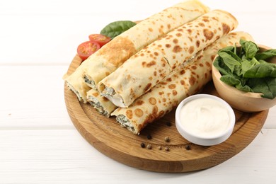 Photo of Tasty rolled crepes with cottage cheese and spinach served on white wooden table, closeup