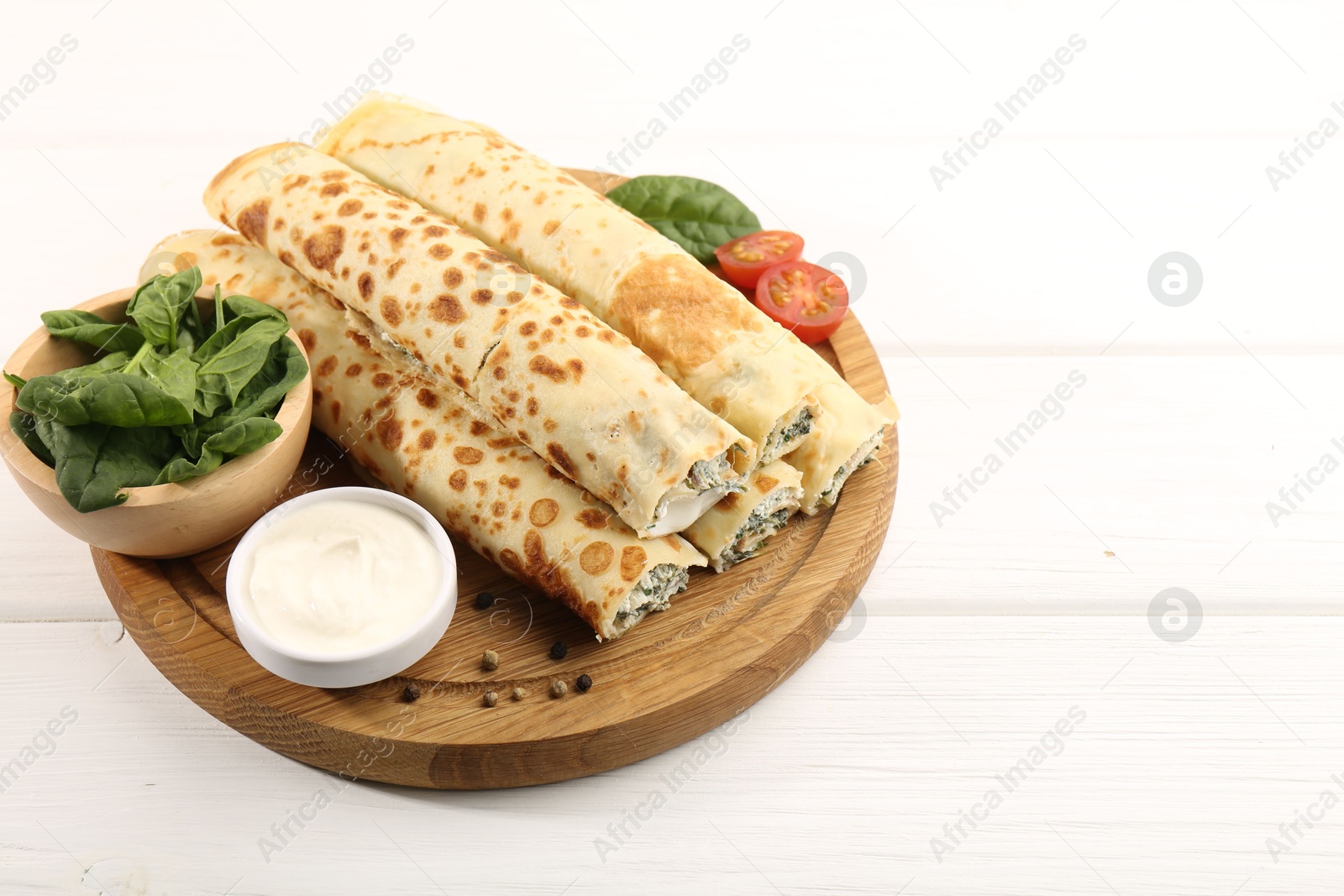 Photo of Tasty rolled crepes with cottage cheese and spinach served on white wooden table, closeup. Space for text