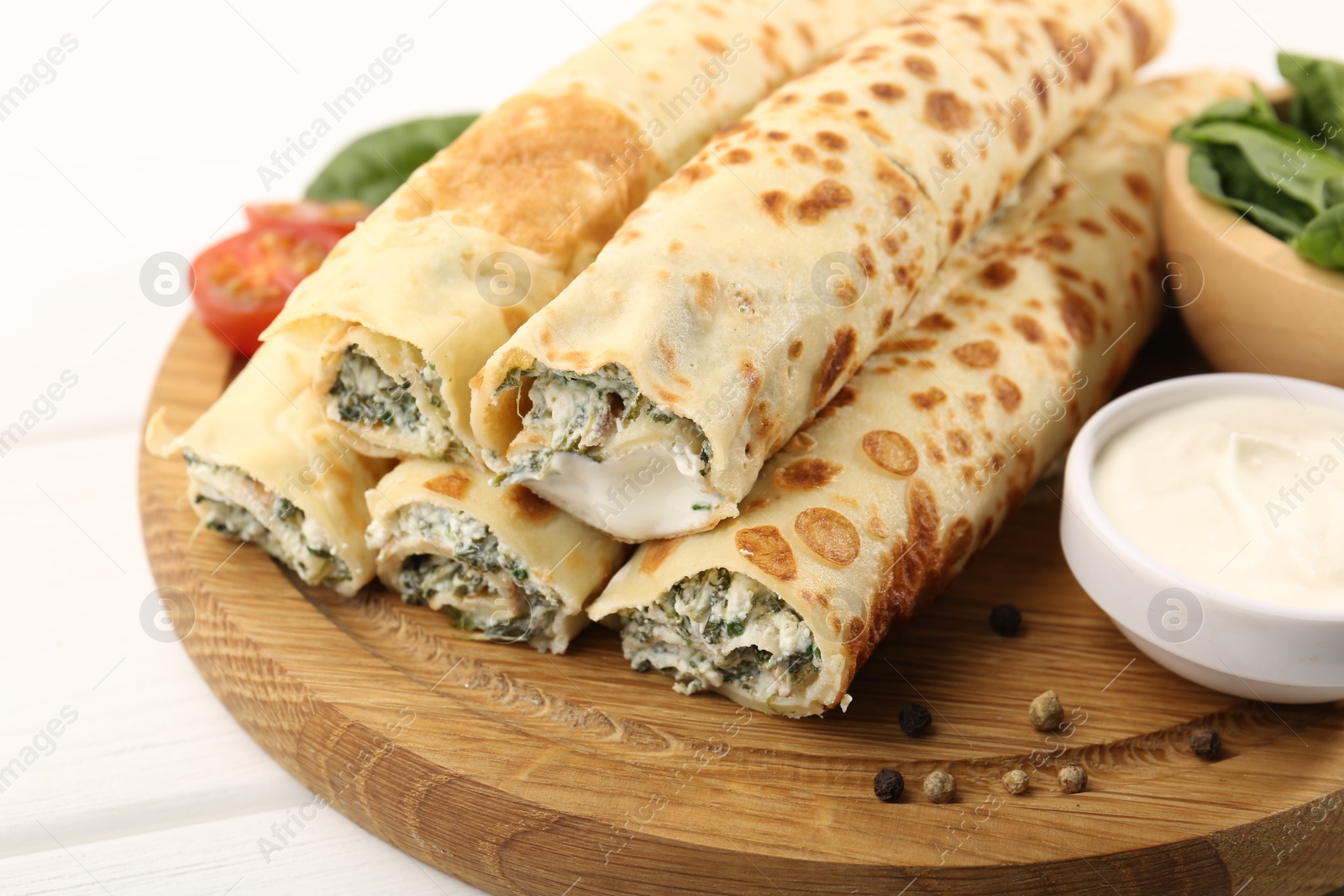 Photo of Tasty rolled crepes with cottage cheese and spinach served on white wooden table, closeup