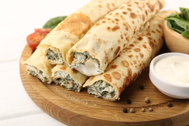 Photo of Tasty rolled crepes with cottage cheese and spinach served on white wooden table, closeup