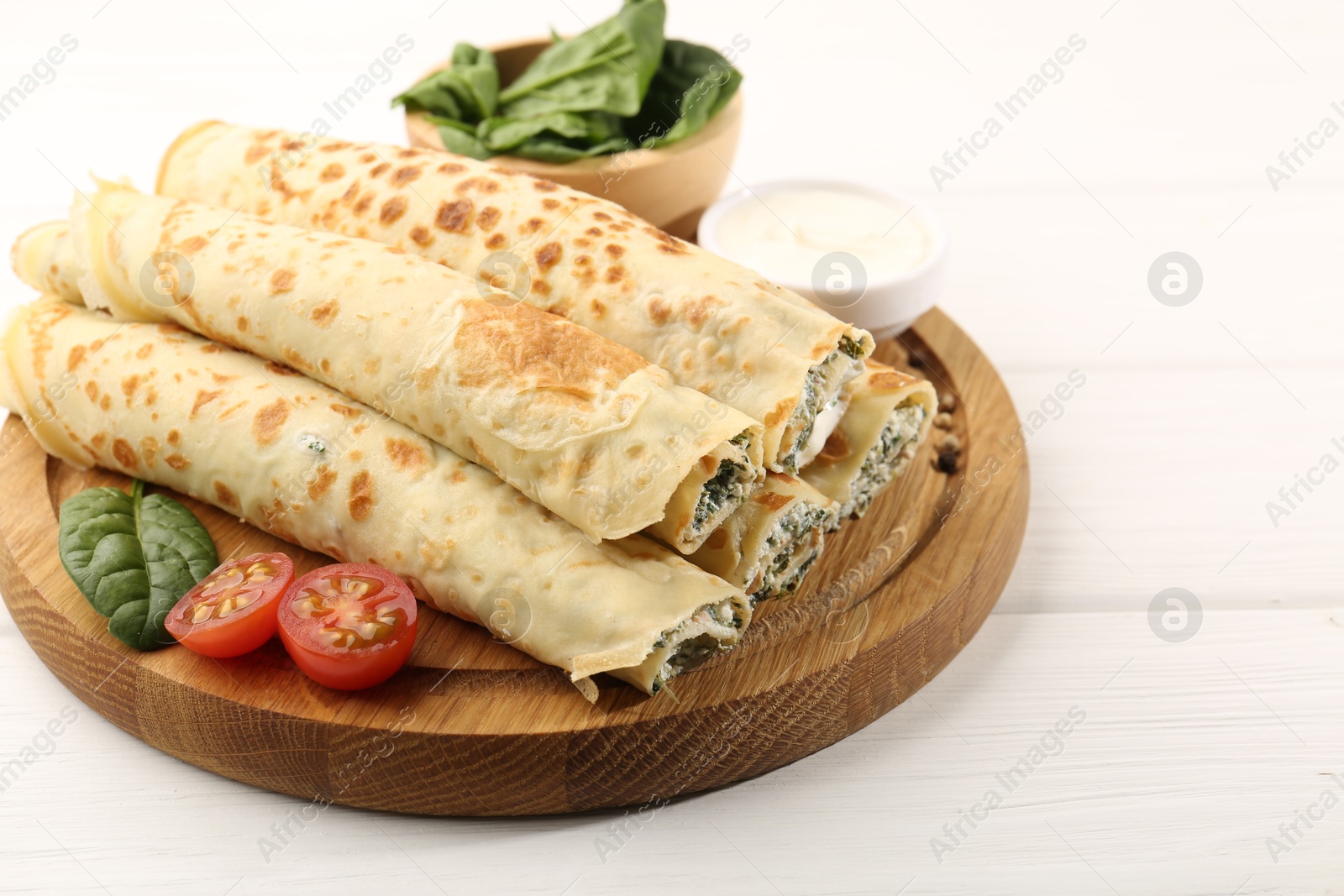 Photo of Tasty rolled crepes with cottage cheese and spinach served on white wooden table, closeup. Space for text